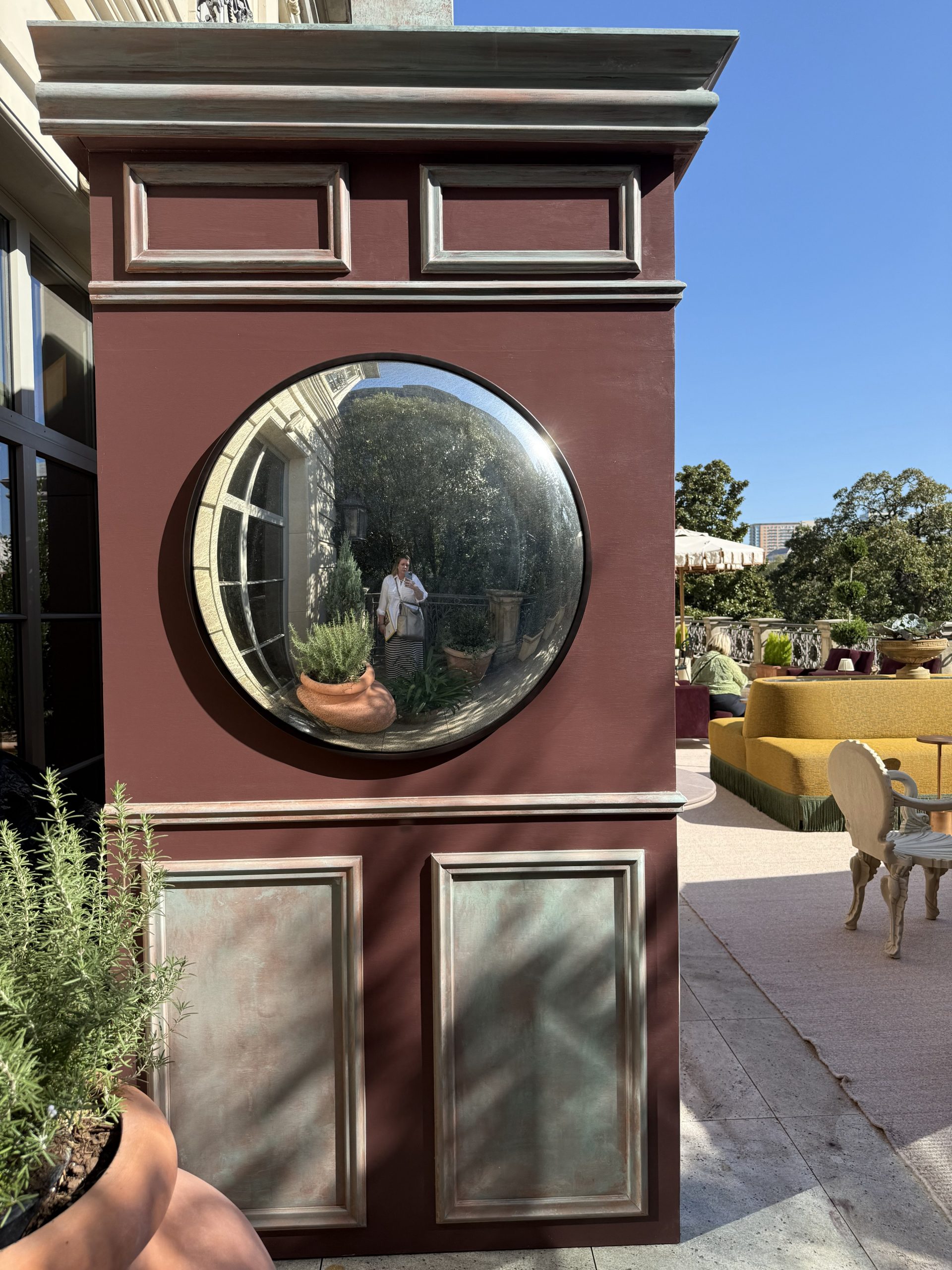 SuAnne Hedgepeth standing beside mirrored sculptures and reflective art pieces on an urban Dallas balcony.
